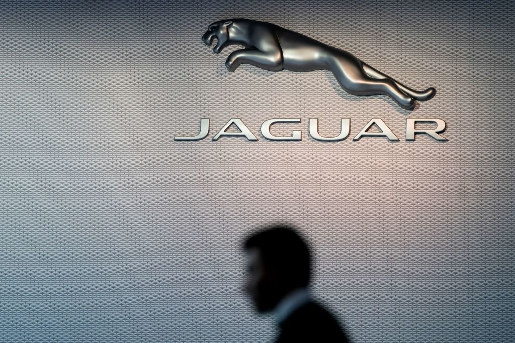 A man passes in front of Jaguar's leaping cat logo at the Brussels Motor Show