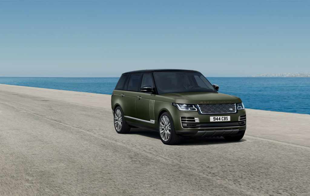 An army green Range Rover sits in the sun by the sea.