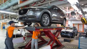 Workers affix parts to the underside of a gray Mazda CX-5 sports utility vehicle (SUV) on the assembly line at the Mazda Sollers Manufacturing Rus LLC plant