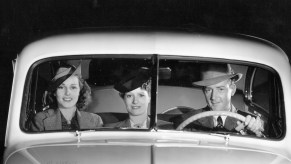 A black-and-white photo of a male driver and two female passengers in the front bench seat of a 1939 Oldsmobile