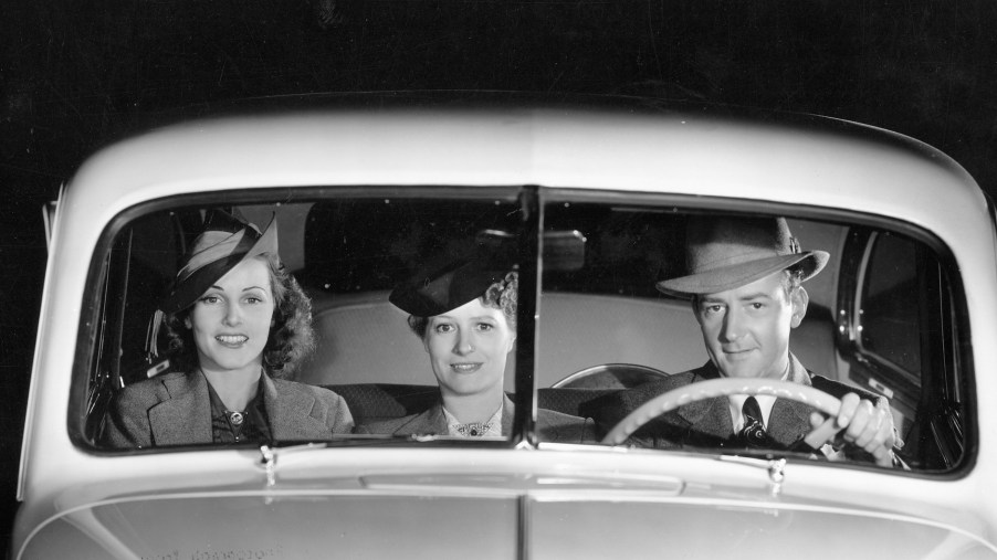 A black-and-white photo of a male driver and two female passengers in the front bench seat of a 1939 Oldsmobile