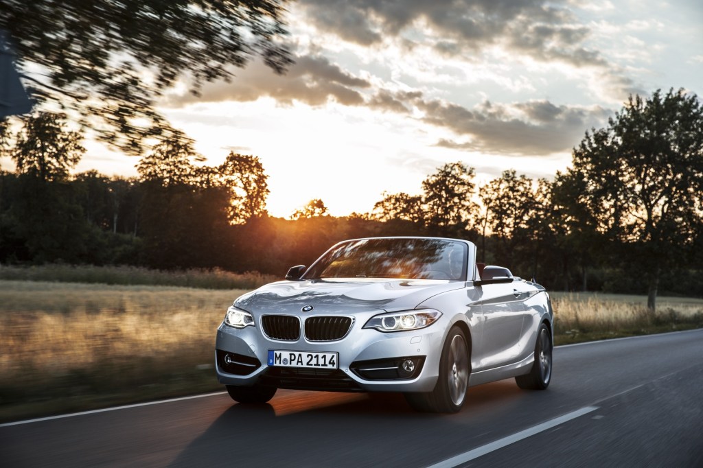 A silver 2 series convertible drives down a road at sunset photographed from the front 3/4