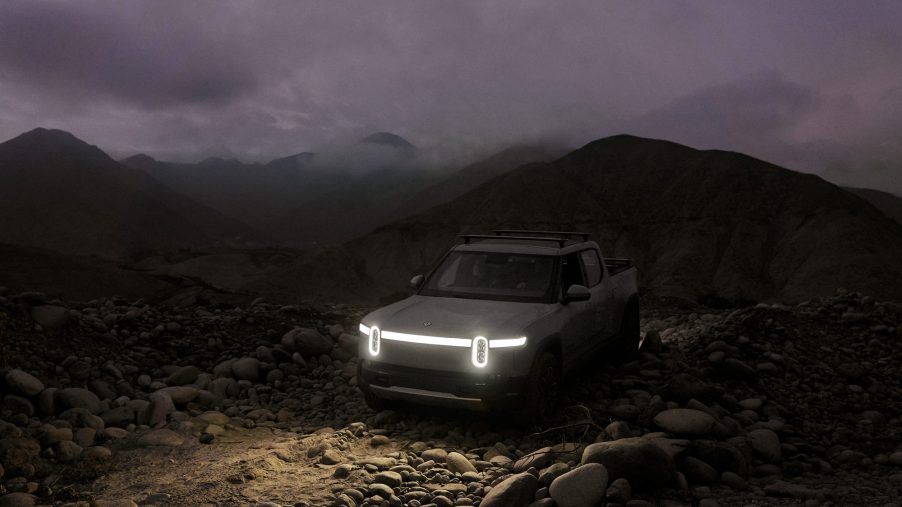 A gray Rivian R1T parked on rocks in front of cloud-shrouded mountains at dusk