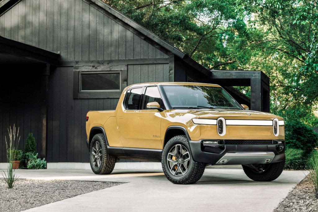 A yellow Rivian R1T parked in front of a house in the forest