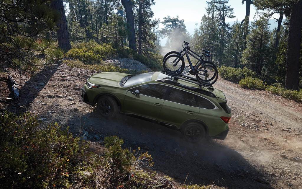 A green 2021 Subaru Outback  driving on a dirt road with bikes on the roof