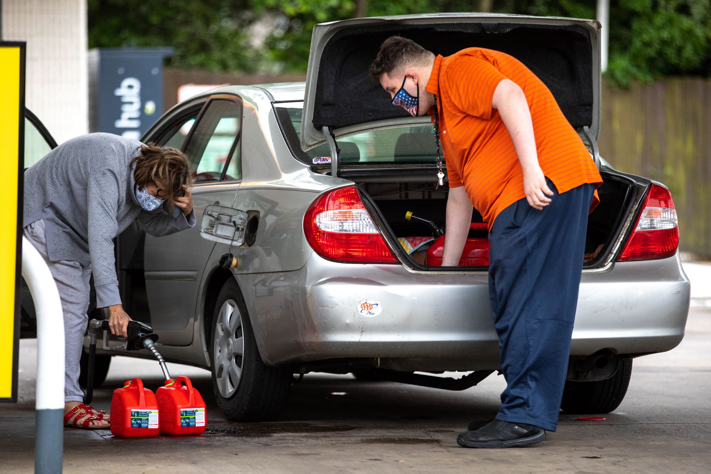Two motorists fill up multiple gas cans and put them in their car