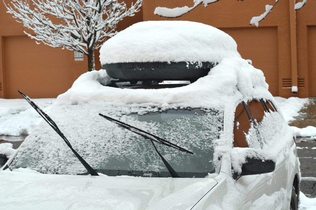   A vehicle with a car-top carrier parked in a driveway is covered with snow and ice after a late autumn storm in New Mexico.