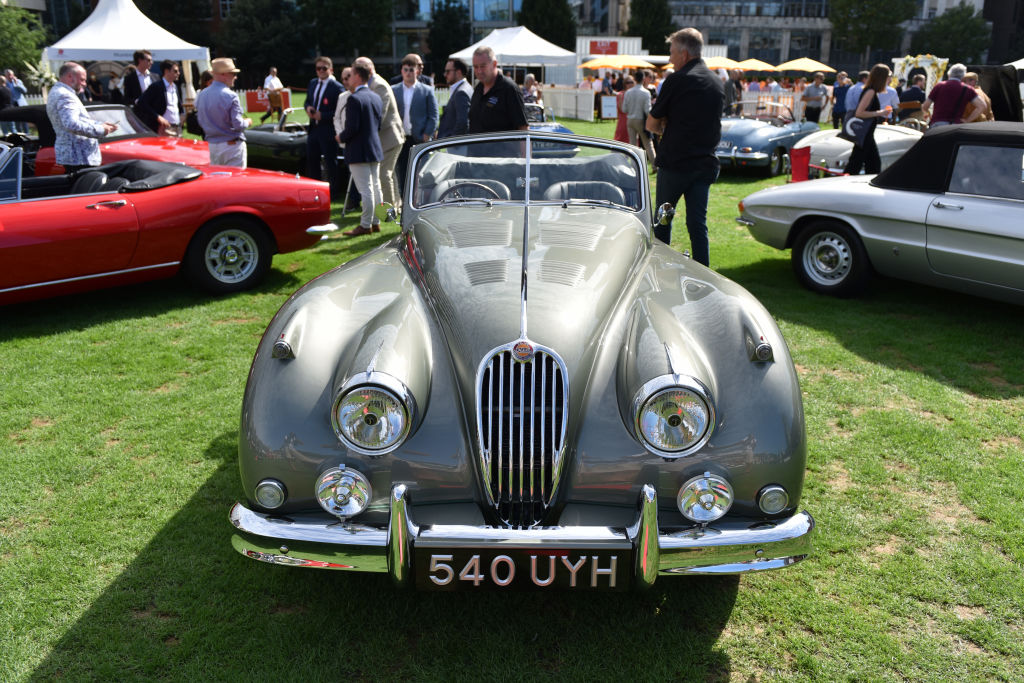 A Jaguar XK140 in silver on the grass at a concours event.