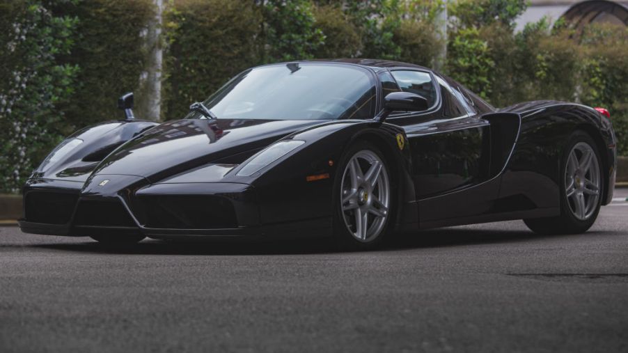 A black Ferrari Enzo sits in the shade against a row of green hedges