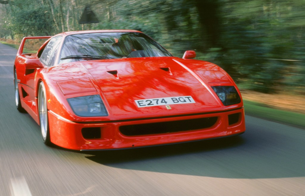 A red Ferrari F40 drives down a forested street, photographed from the nose.