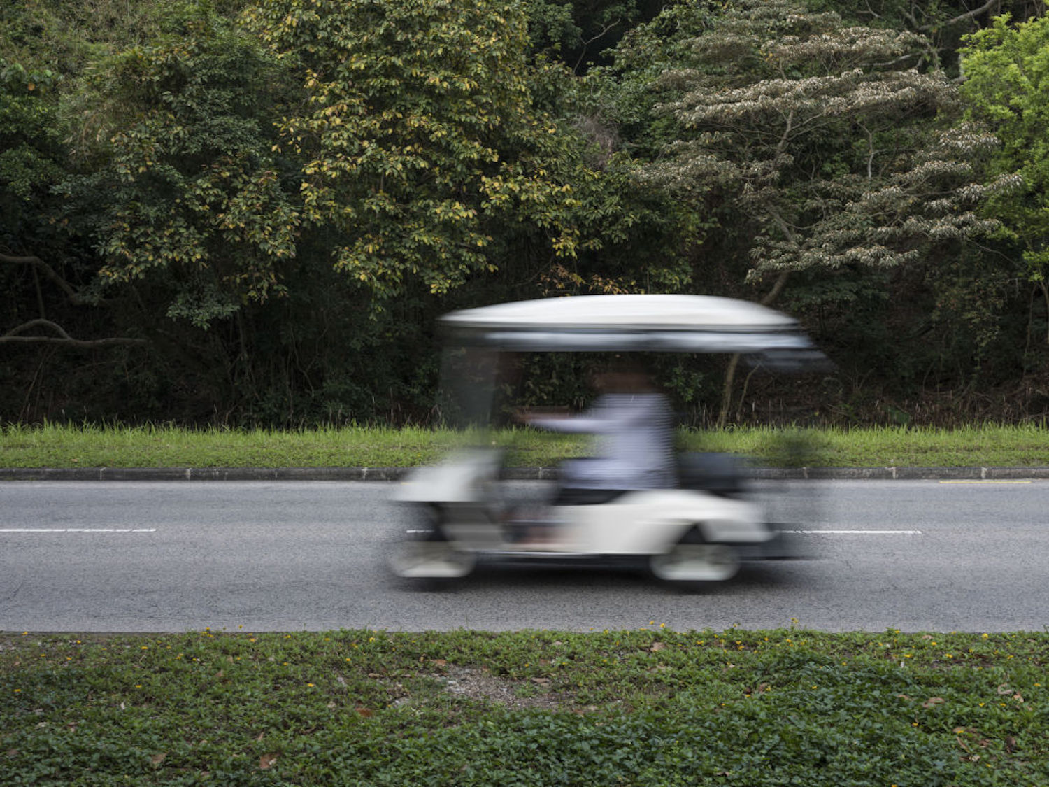 A white golf cart travels on a road