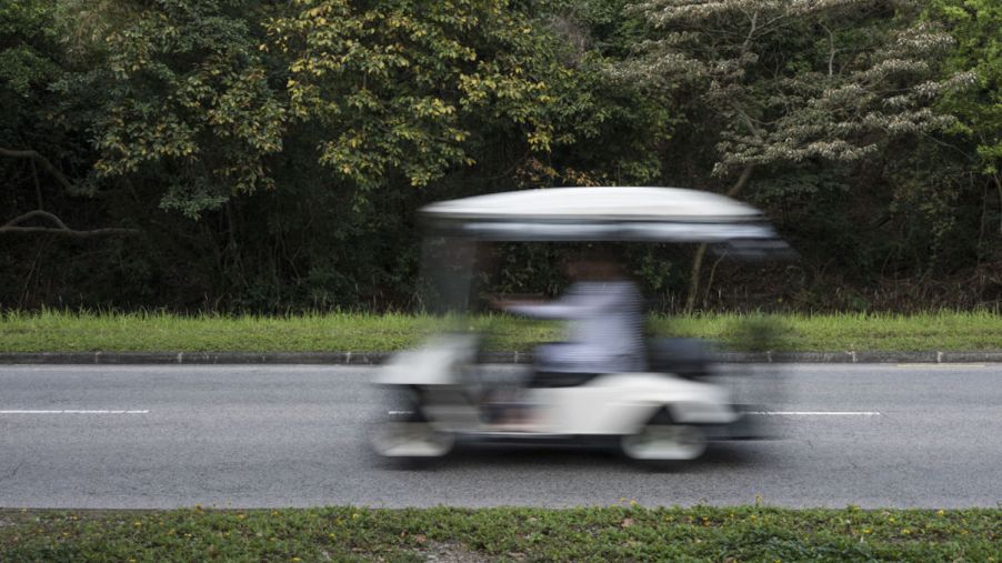 A white golf cart travels on a road