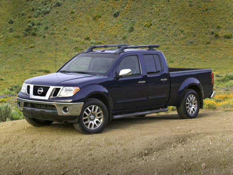 a dark blue 2021 Nissan Frontier parked in the dirt with green hills in the background 