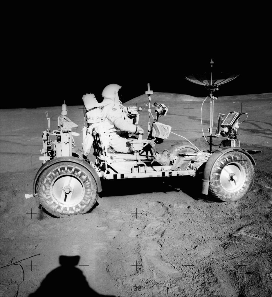 An astronaut drives a moon buggy on the surface of the moon. 