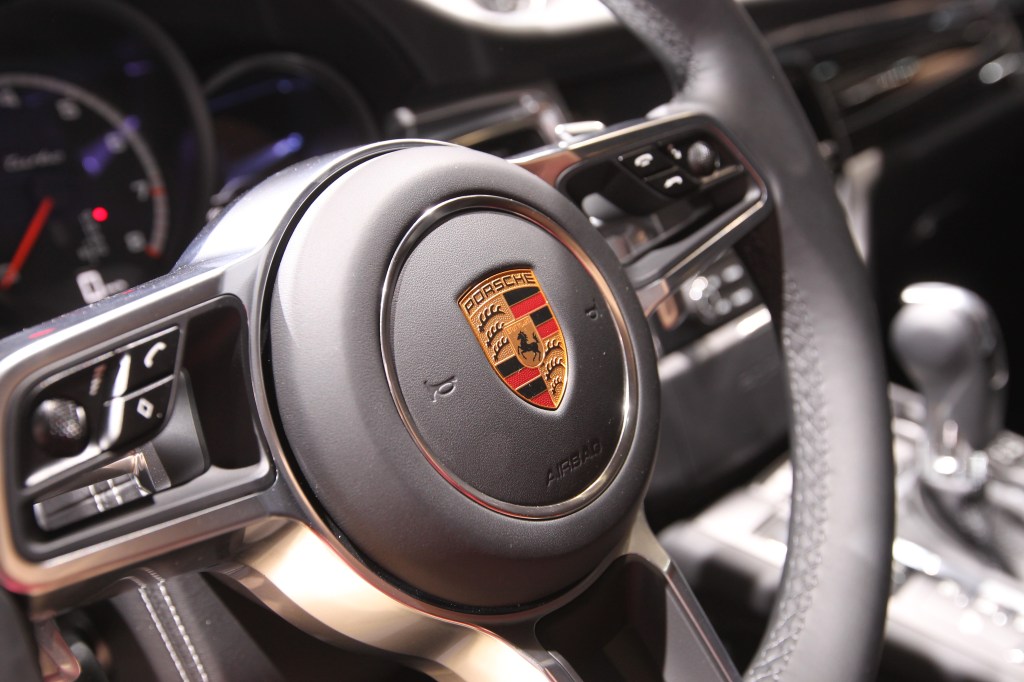 The black, leather-wrapped wheel of a Porsche Macan photographed from the exterior looking in.