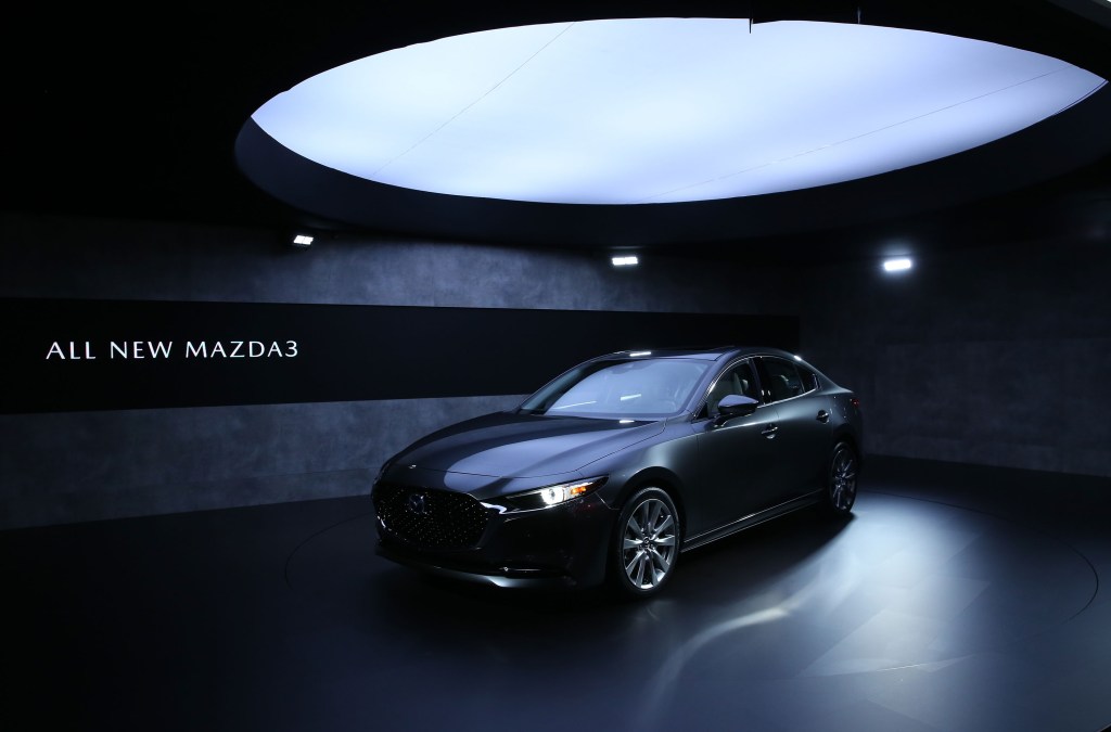A top Consumer Reports pick, the 2020 Mazda3 in grey is shown under a light box at the L.A Auto Show