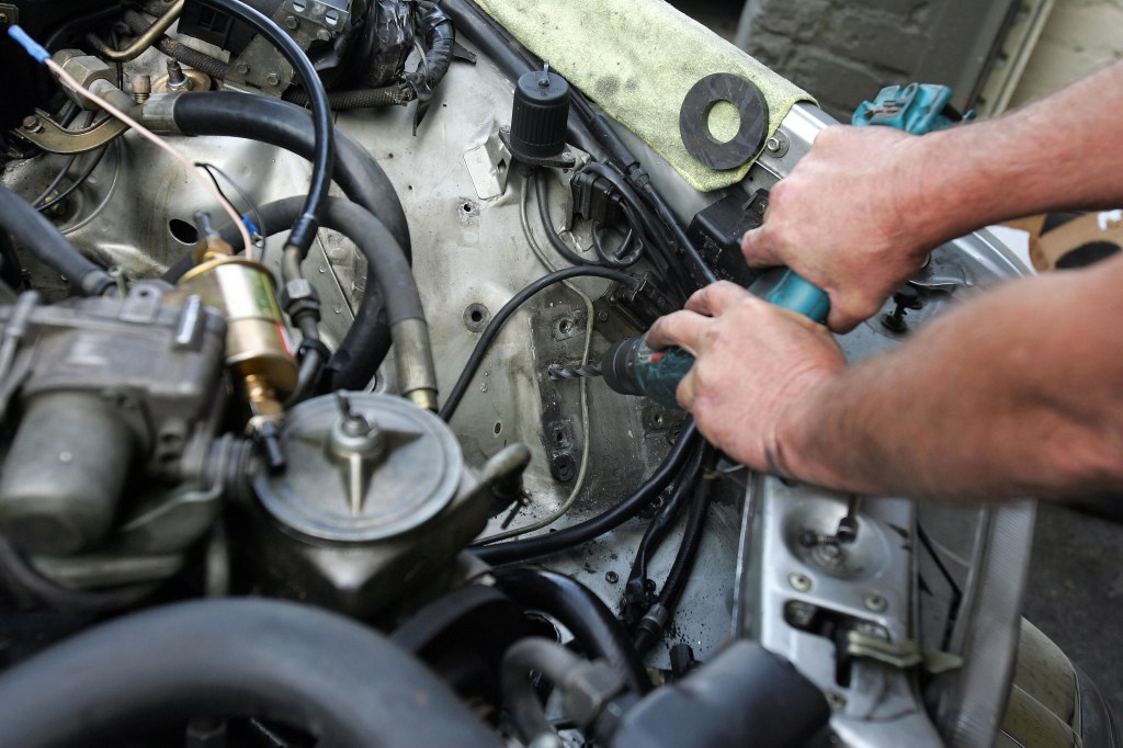   Mechanic Mike Ackerman drills holes under the hood of a car. 