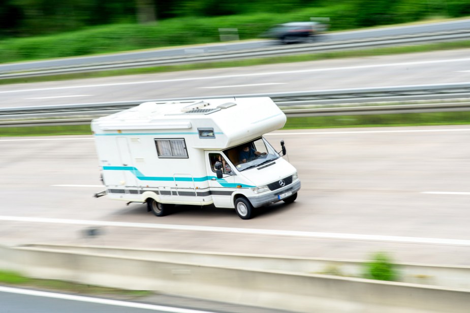 A white and turquoise-blue Mercedes-Benz RV traveling on a highway