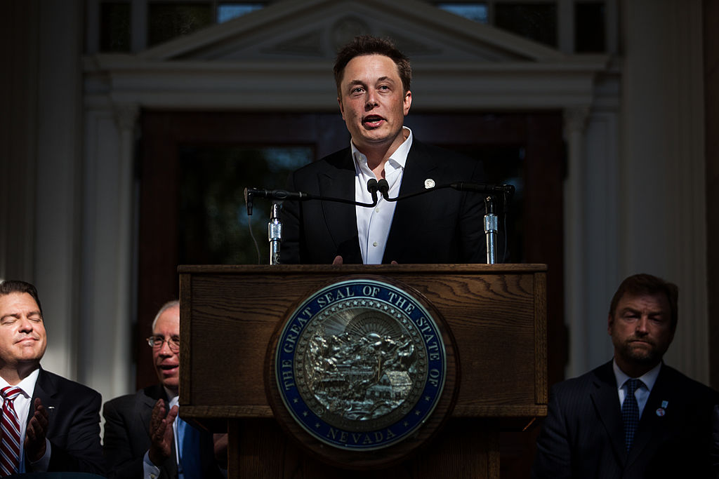 Elon Musk stands at a podium with the Nevada State Seal on it, speaking to a crowd