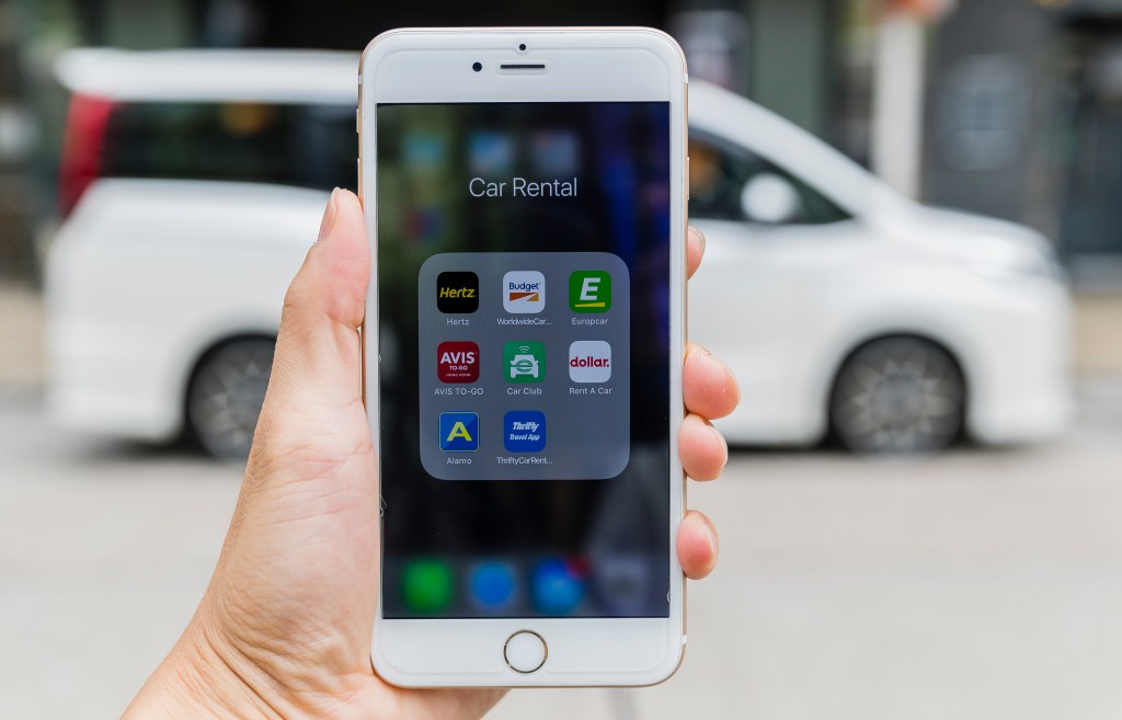 A smartphone with the icons for the car rental apps from Hertz, Budget Rent a Car, Europcar, Avis Rent a Car, Enterprise Rent-A-Car, Dollar Rent A Car, Alamo Rent a Car, and Thrifty Car Rental. 