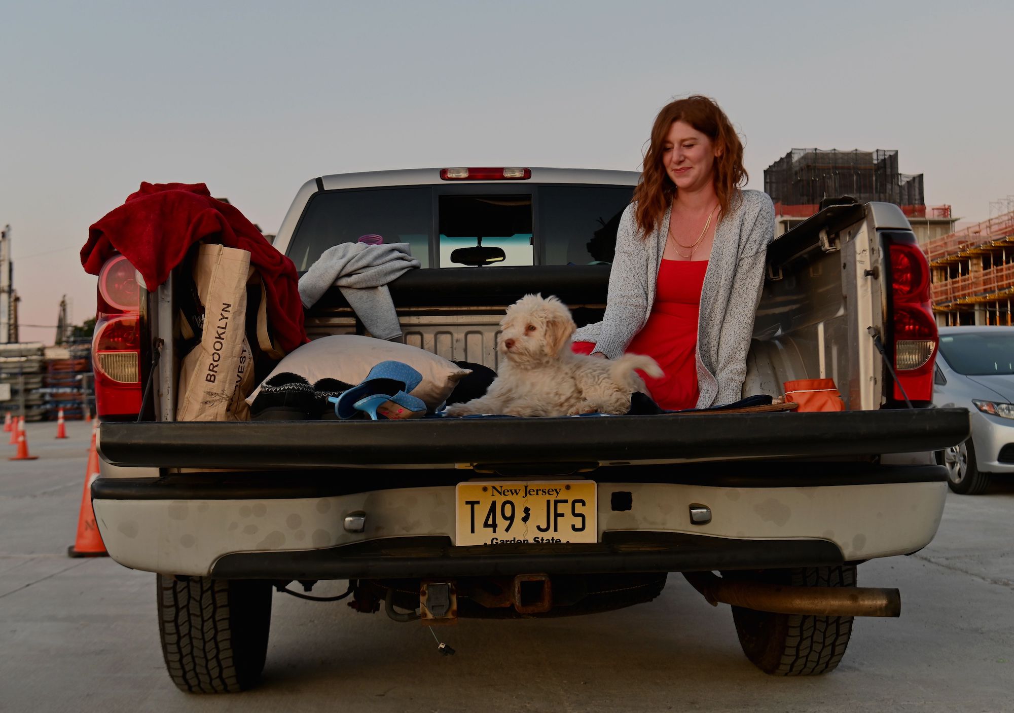 A woman sits in the bed of a pickup truck with a dog