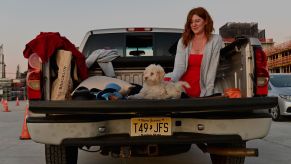 A woman sits in the bed of a pickup truck with a dog