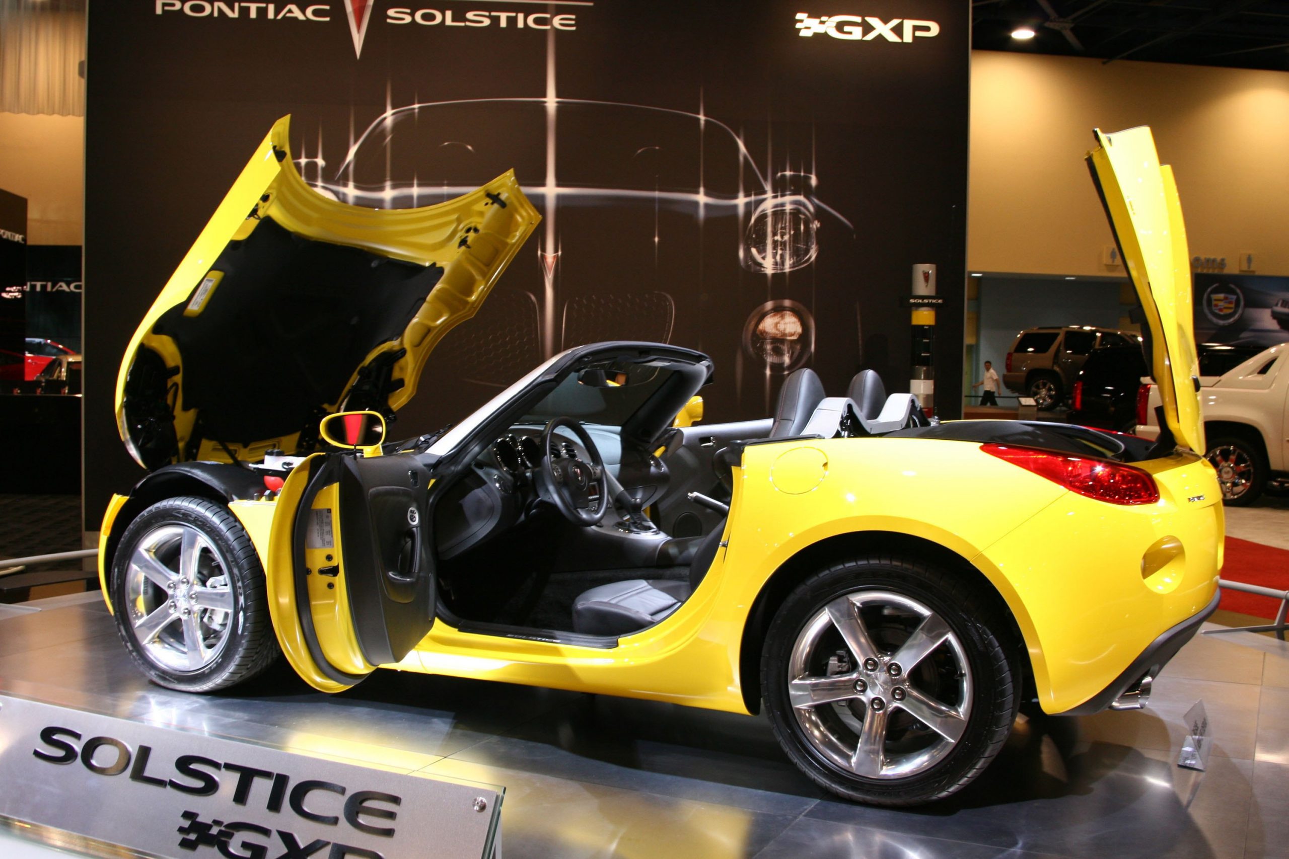 a yellow pontiac solstice sports car on display with the front and rear hatch open