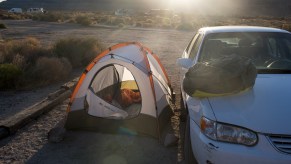 A camper pitches a tent next to his car to block winds from blowing it away in Mojave National Preserve on May 6, 2021, in California