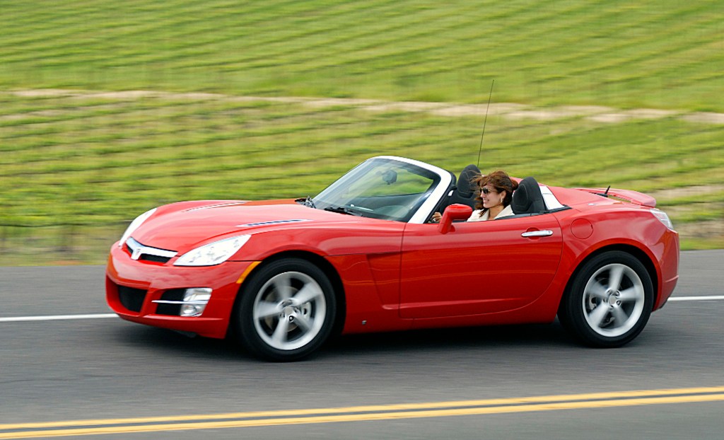 A red saturn sky convertible with the top down driving down the highway