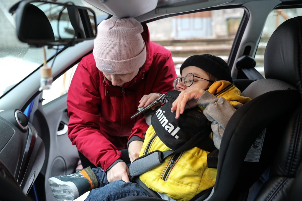 A mother buckles her son into the car