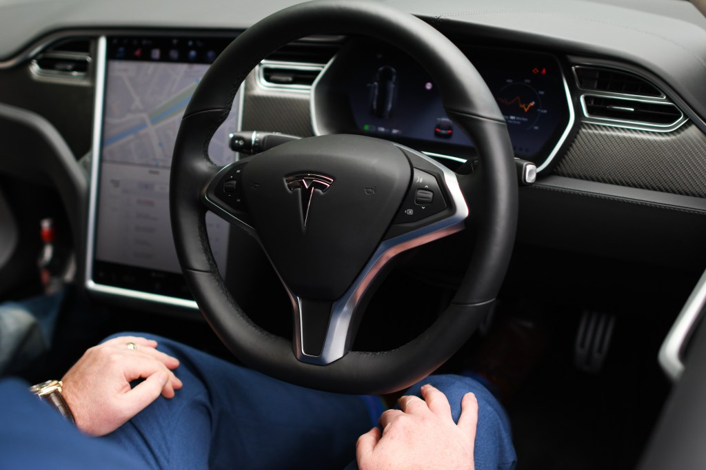 A driver rests their hands on their knees as the Tesla Model S they sit in drives itself autonomously. 