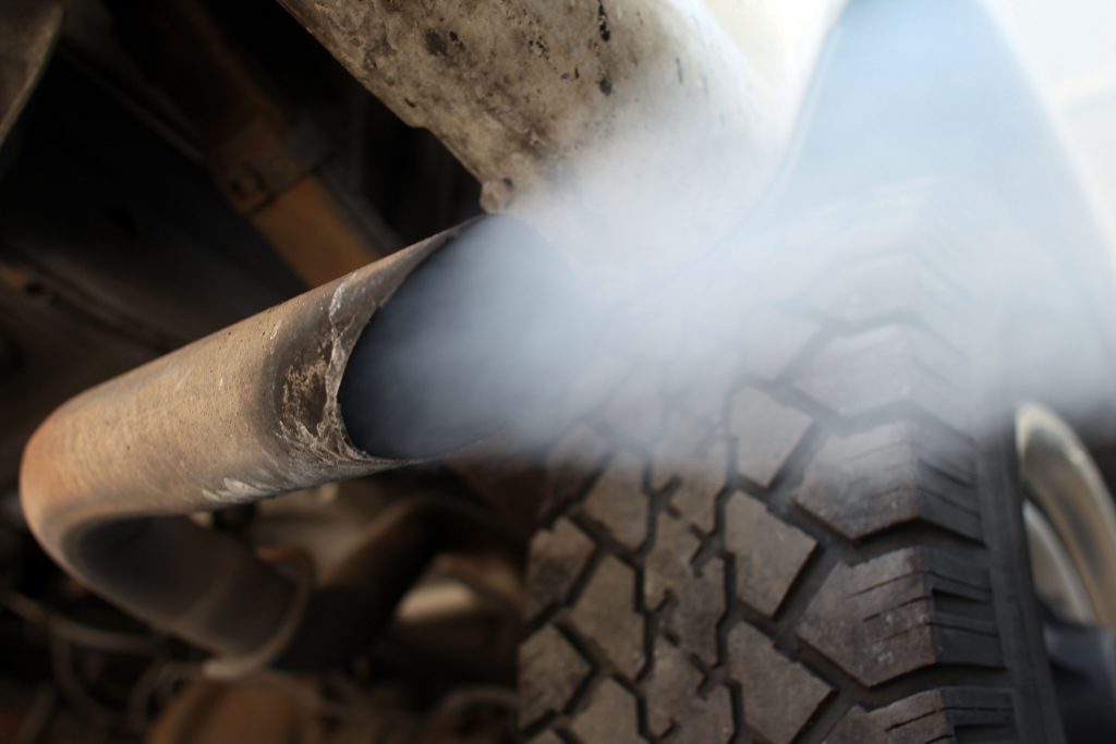Exhaust flows out of the tailpipe of a vehicle at "Mufflers 4 Less." 