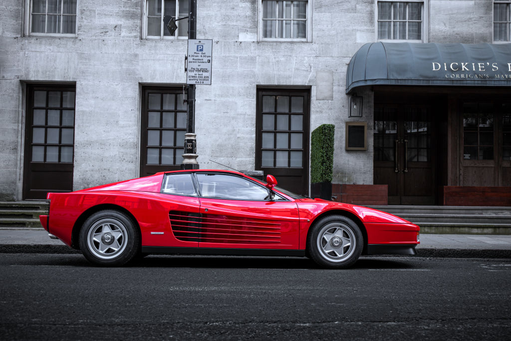 A red Ferrari Testarossa sits outside on a street in London, photographed in profile
