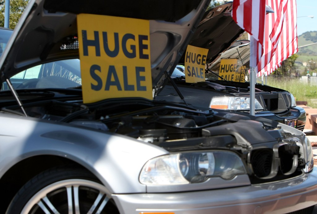 Signs advertising sales, propped up under the hoods of used cars