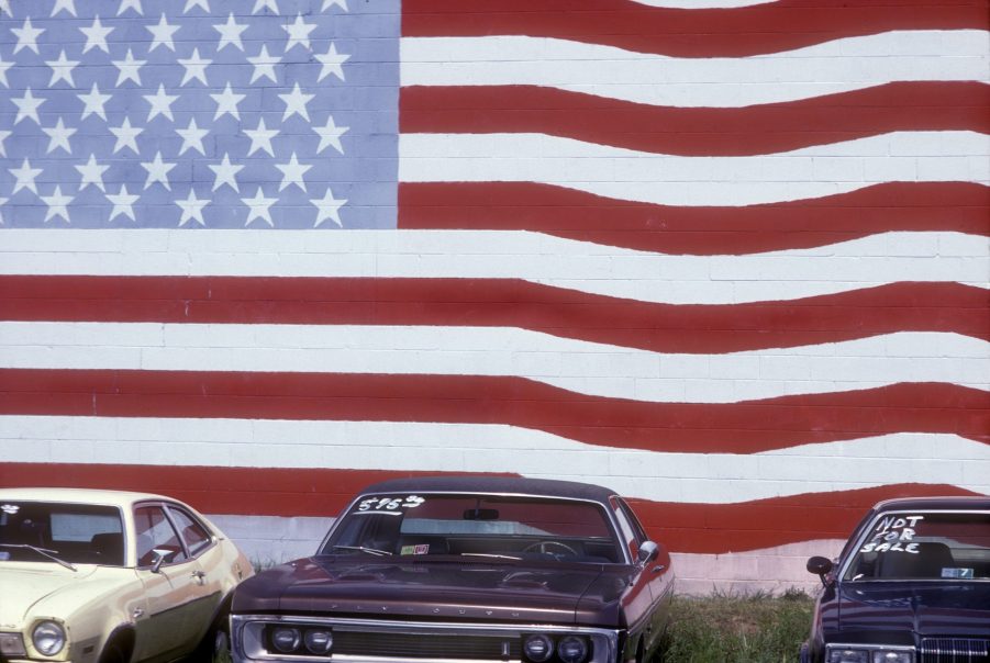 Used cars for sale in front of a wall painted with an American flag mural