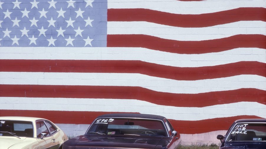 Used cars for sale in front of a wall painted with an American flag mural