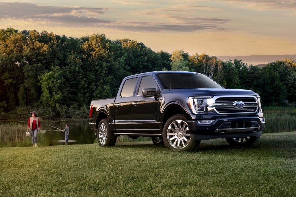 A navy blue 2021 Ford F150 in front of a lake while a man fishes and a woman carries a tackle box.