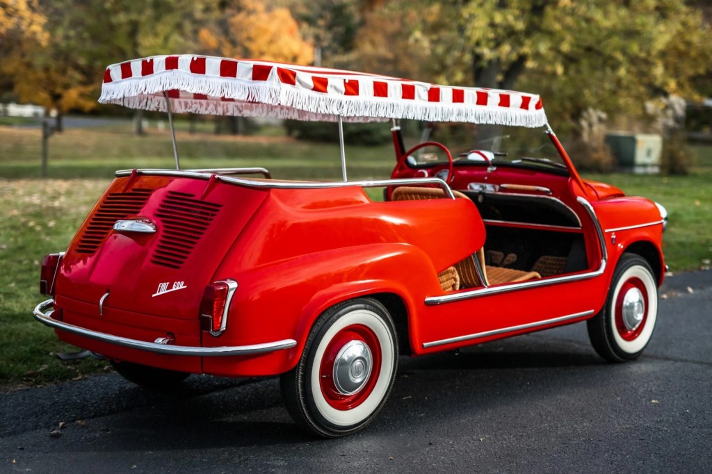 The rear 3/4 view of a red 1958 Fiat Jolly 600 parked on a driveway