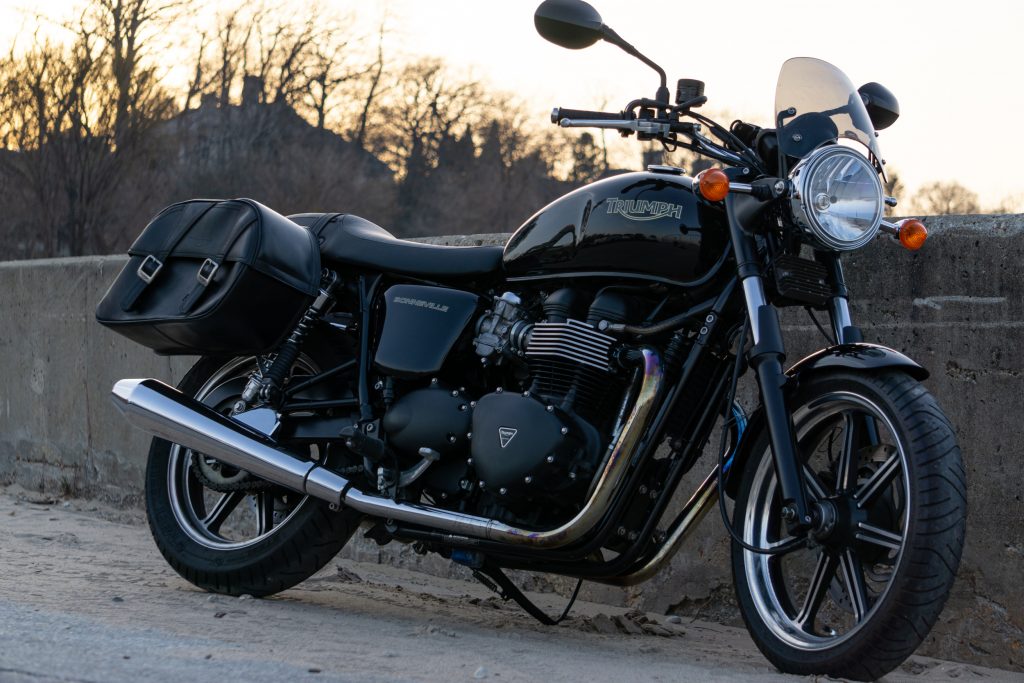 A black 2009 Triumph Bonneville with black leather saddlebags next to a concrete beach barrier
