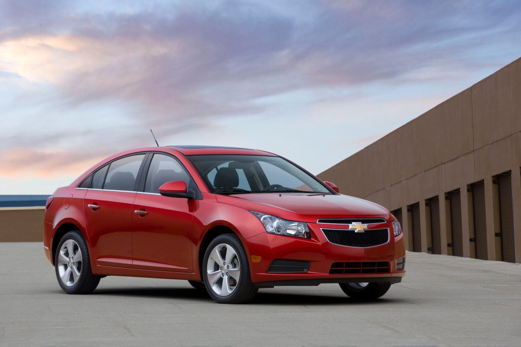 A red 2011 Chevrolet Cruze parked on a roof with a blue sky and wispy clouds in the background