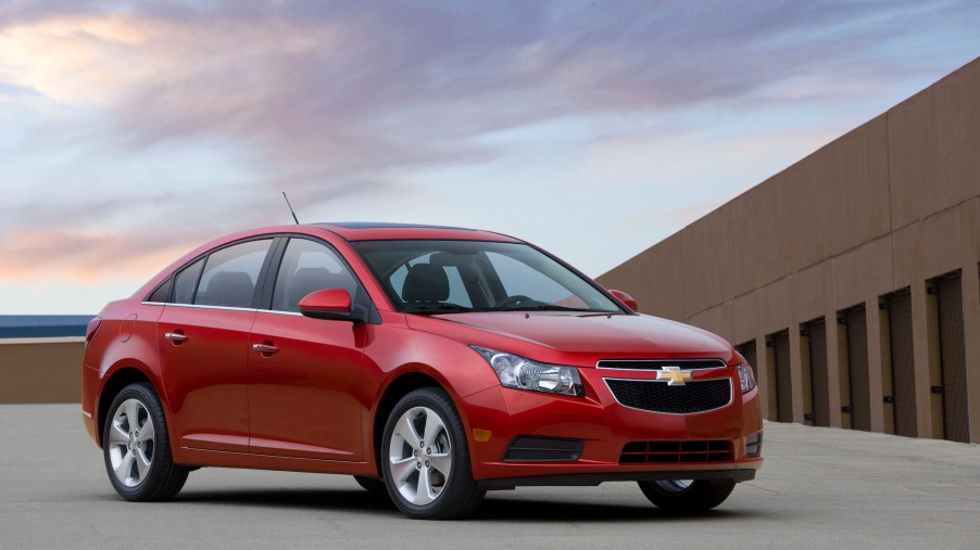 A red 2011 Chevrolet Cruze parked on a roof with a blue sky and wispy clouds in the background