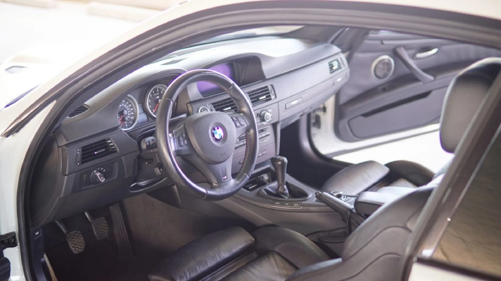 The black-leather-upholstered front seats and carbon-fiber-trimmed dashboard of a 2012 BMW M3 Competition Coupe seen through the open doors