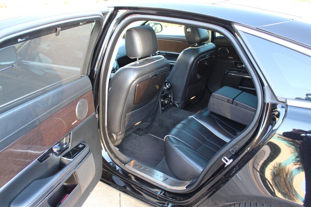 The black-leather-upholstered and wood-trimmed interior of a black 2012 Jaguar XJL Supercharged seen through the rear door
