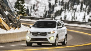A white 2017 Kia Sorento SUV travels through a curve in a two-lane highway through snow-covered mountains