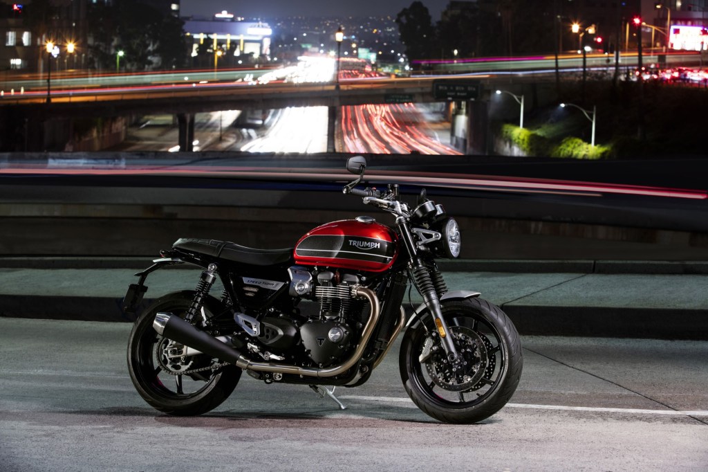 The side view of a red-and-black 2019 Triumph Speed Twin on a bridge over a highway at night