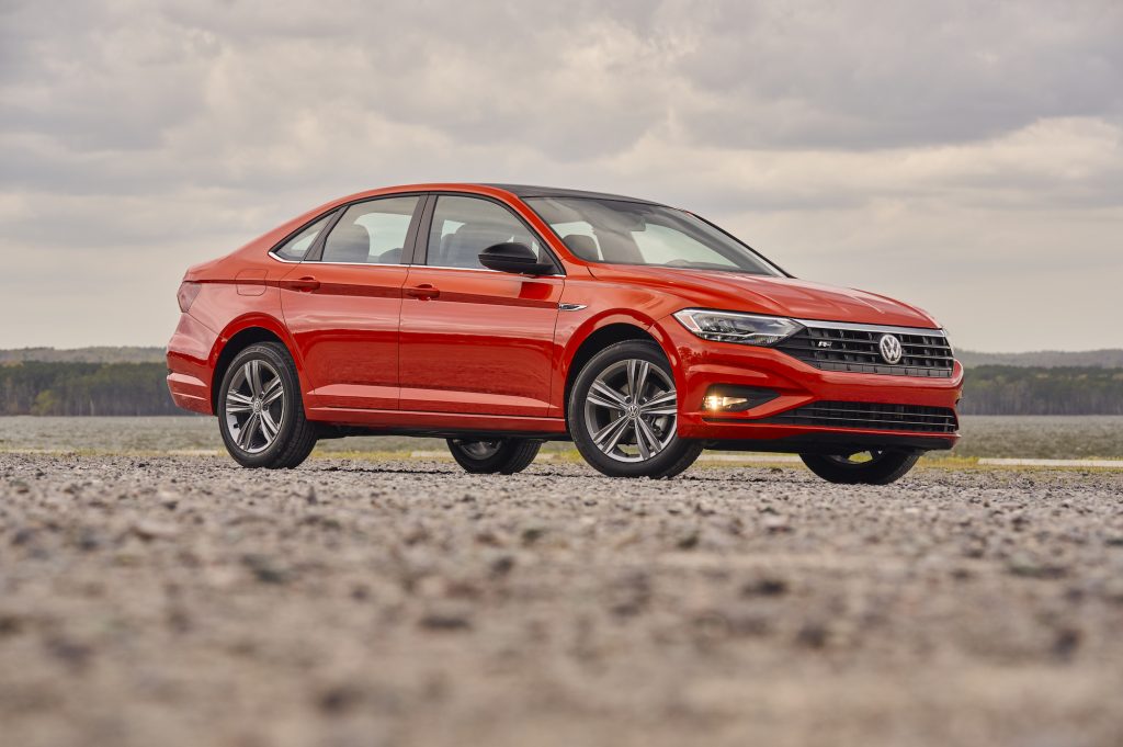 A red 2019 Volkswagen Jetta compact sedan parked on gravel on a cloudy day with mountains in the distance