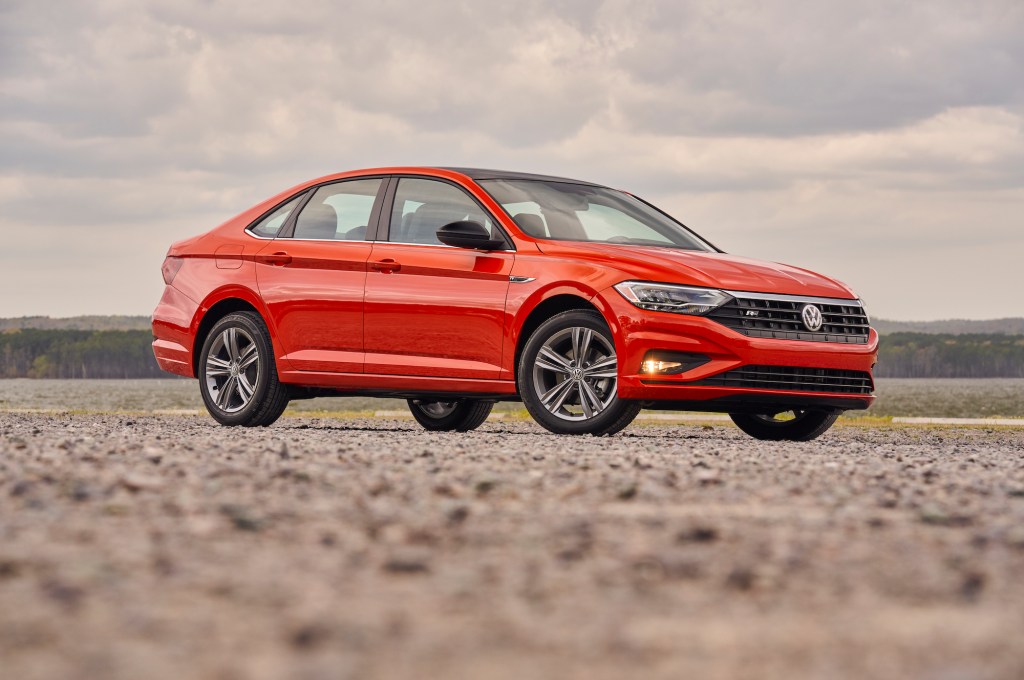 A red 2019 Volkswagen Jetta compact sedan parked on gravel on a cloudy day with mountains in the distance