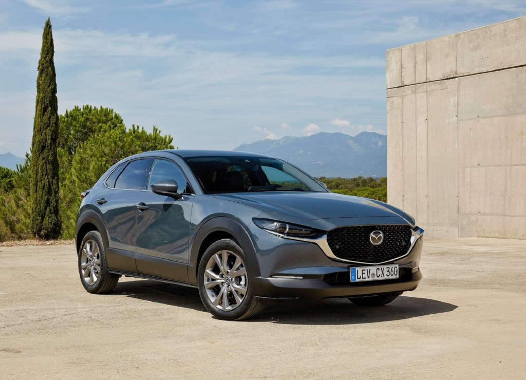 A silver-gray 2020 Mazda CX-30 by a building overlooking tree-covered mountains and hills