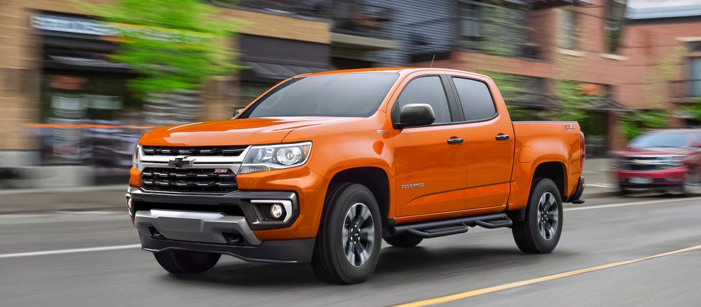 An orange Chevy Colorado pickup truck driving in the city 