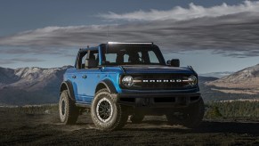 A blue 2021 Ford Bronco 4-Door Black Diamond with Sasquatch Package and light bar on a rocky mountain